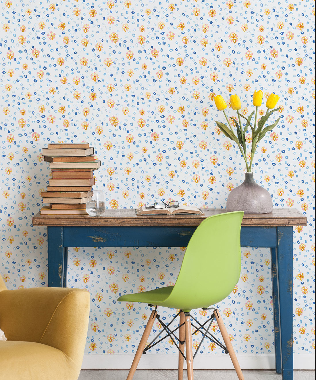 Al Hadiqa Wallpaper • Dainty Floral Design • Desk with books stacked on the left and a lime green chair in front with yellow tulips in a vase on the right side of the desk. • Milton & King Europe